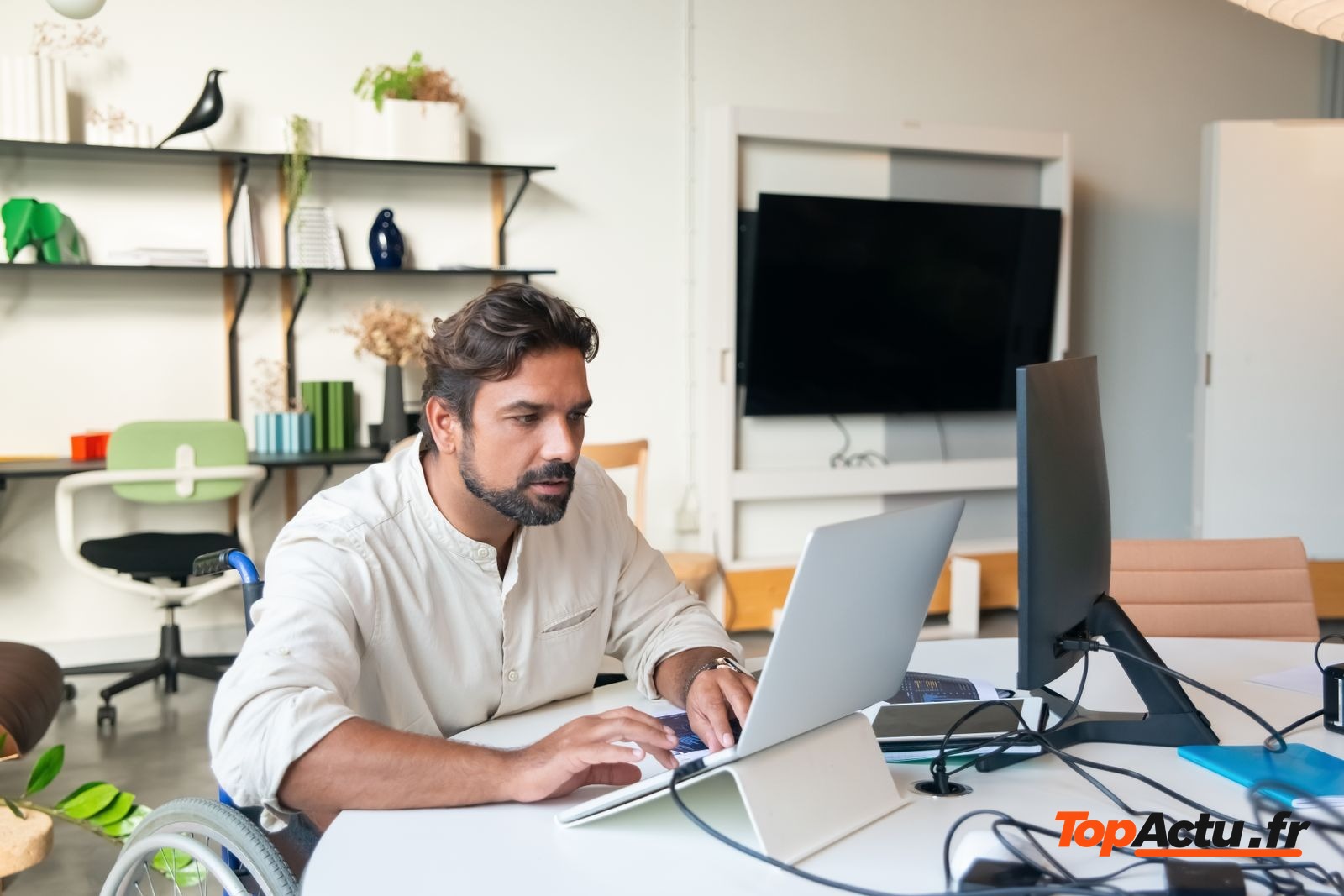 Homme en fauteuil roulant qui travaille sur un ordinateur portable dans un bureau lumineux