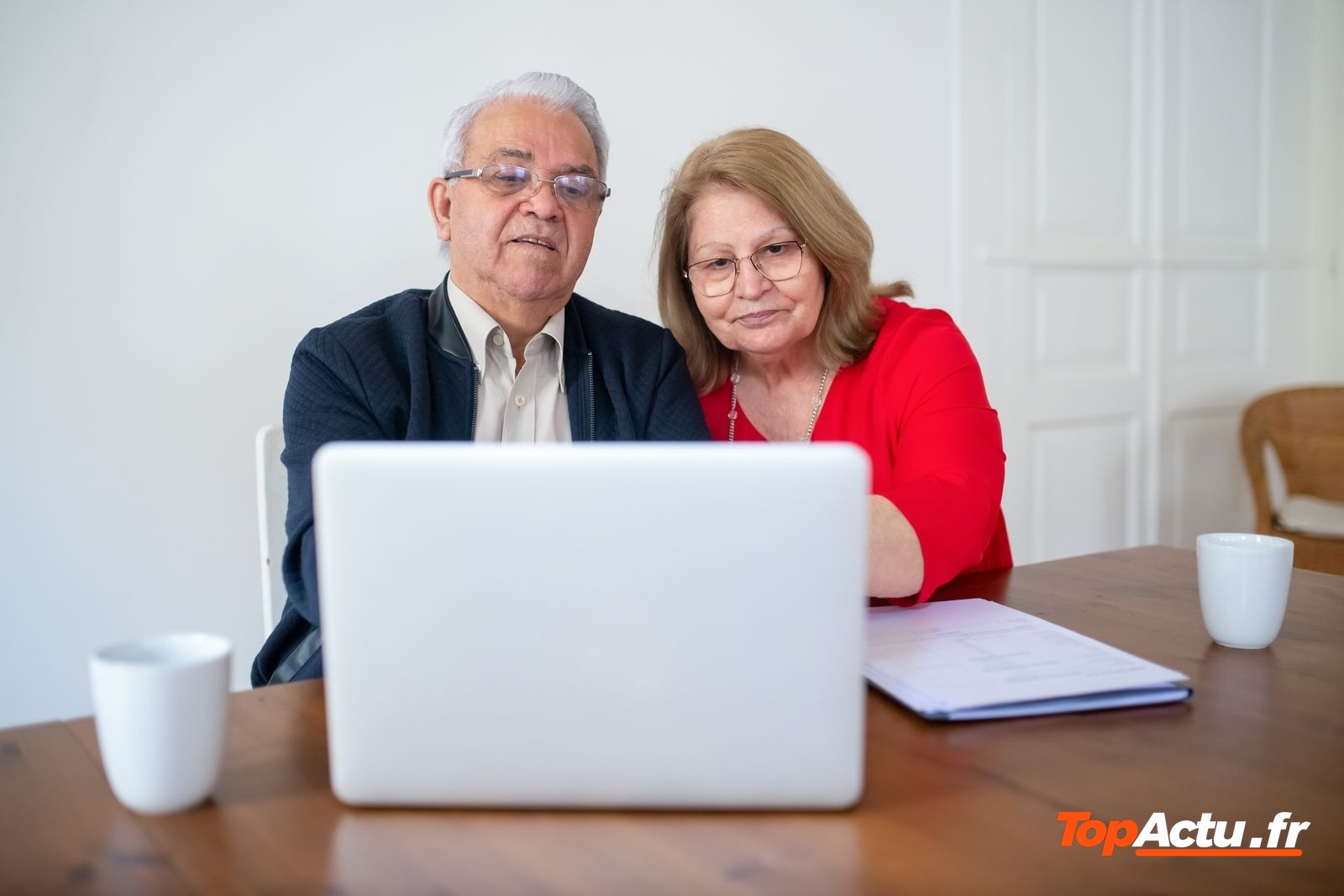 Couple de seniors devant un ordinateur portable, avec des documents posés sur la table