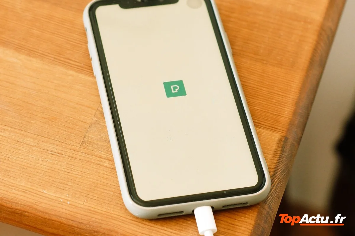 Un smartphone en charge posé sur une table en bois, branché à son câble