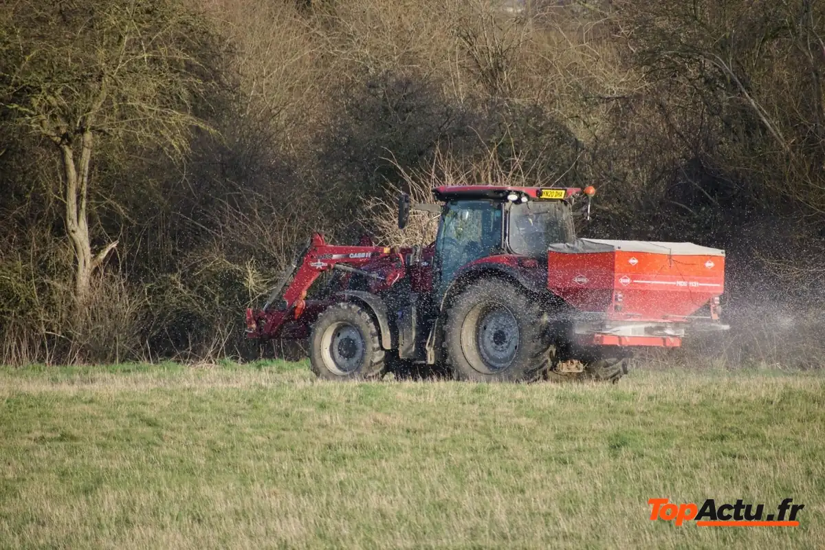 Tracteur rouge qui épand de l'engrais dans un champ en bordure de bois
