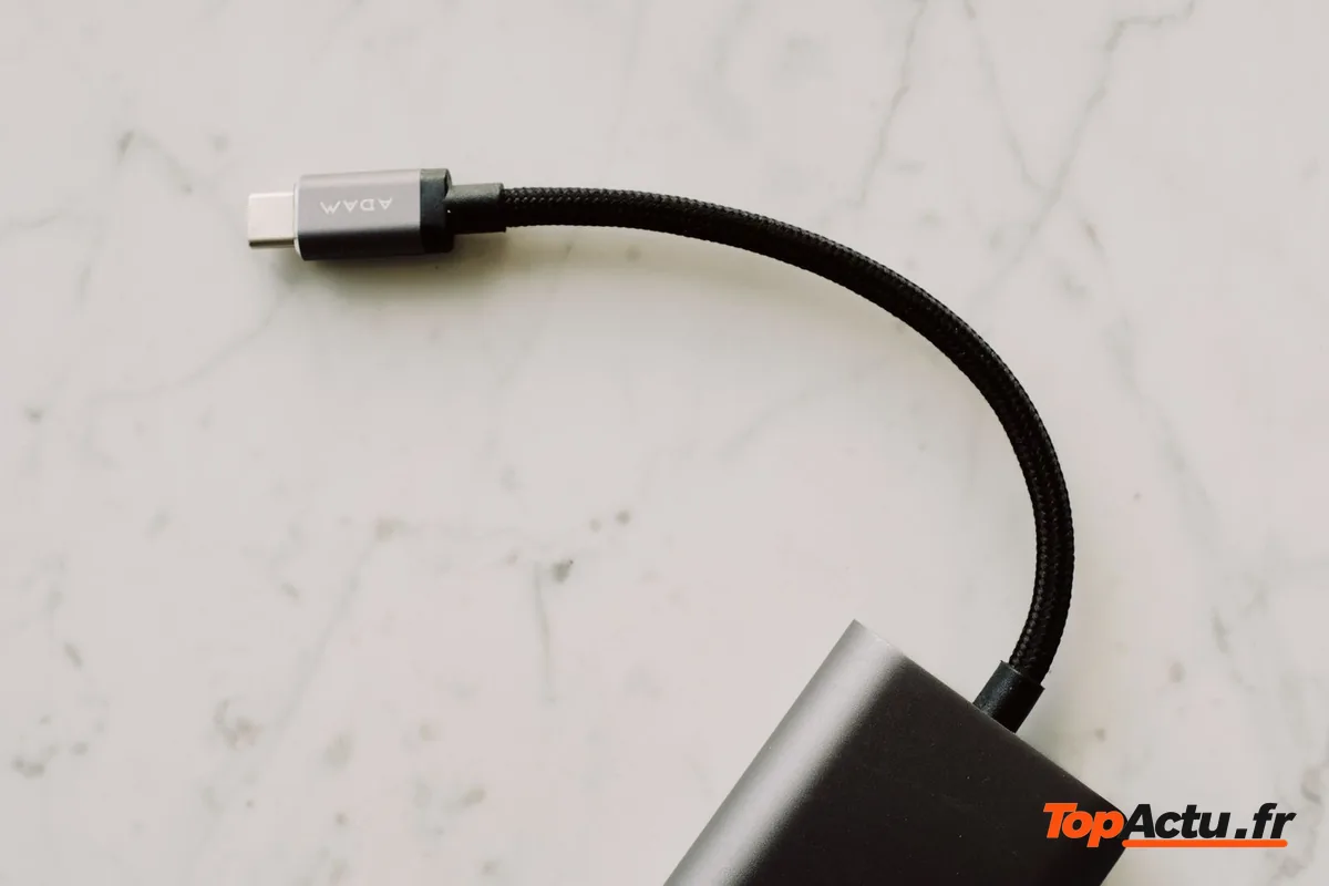 Un câble USB-C tressé relié à un adaptateur gris posé sur un plan de marbre blanc