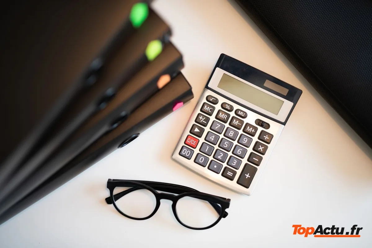 Une calculatrice et des lunettes posées sur un bureau, à côté de dossiers