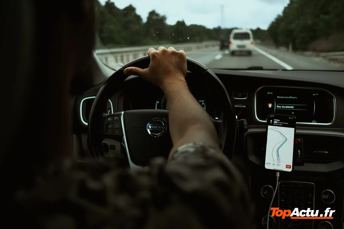 Main sur le volant d'une voiture, smartphone fixé au tableau de bord, route devant