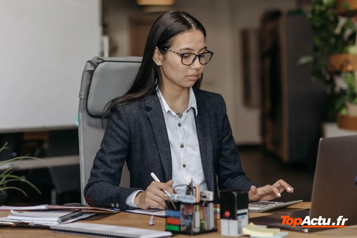 Une employée assise à son bureau devant un ordinateur portable et des documents