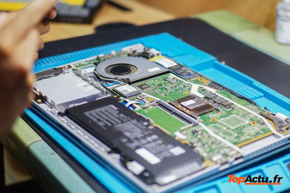 Un ordinateur portable ouvert sur un tapis de réparation, la carte mère et la batterie apparentes