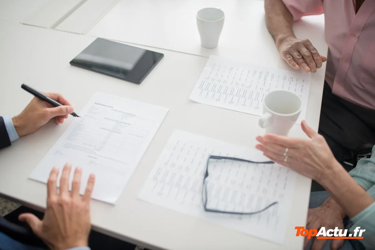 Des mains qui signent un document posé sur une table, à côté d'un autre papier