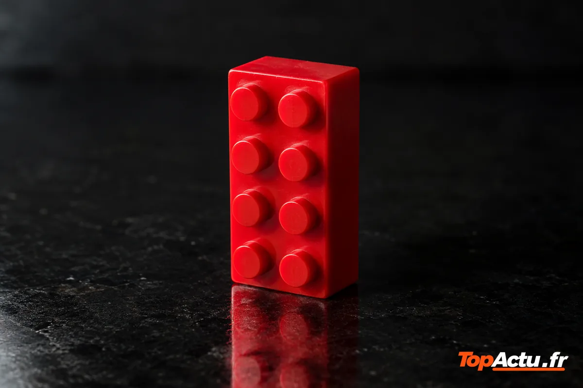 Une brique de construction rouge à tenons sur une surface sombre et brillante, éclairée de côté