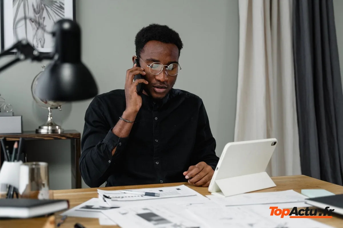 Un homme au téléphone à son bureau, avec des documents et une tablette devant lui