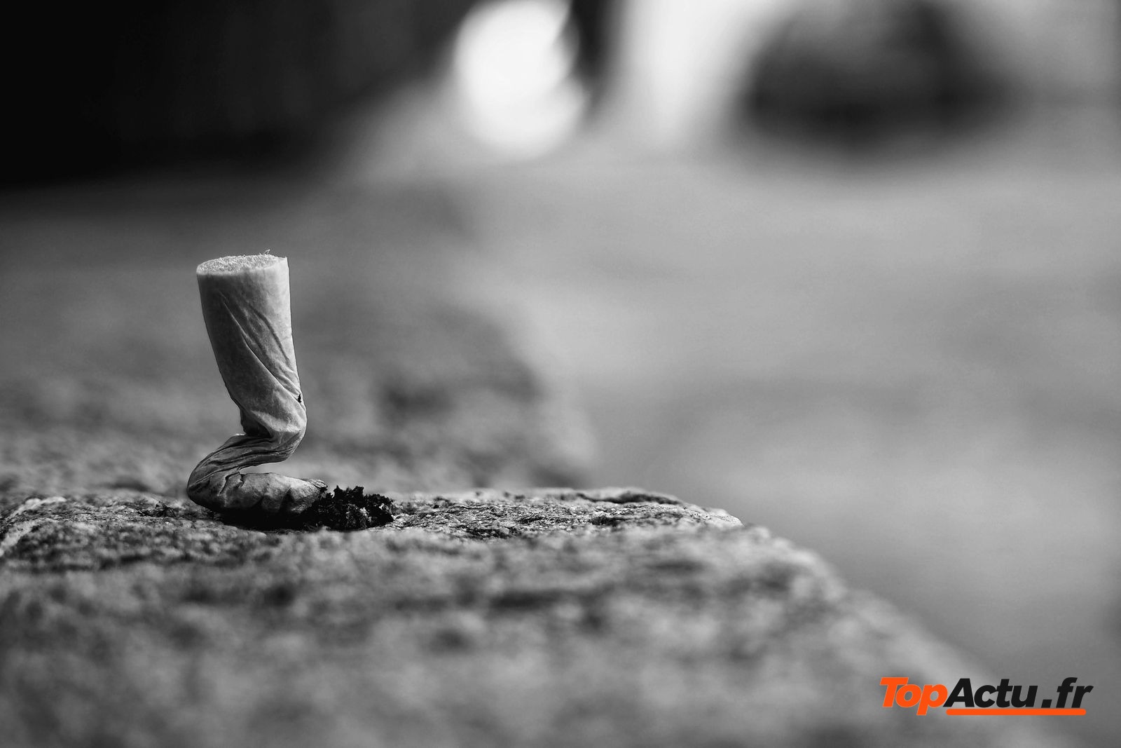Mégot de cigarette posé sur un rebord en pierre, en noir et blanc
