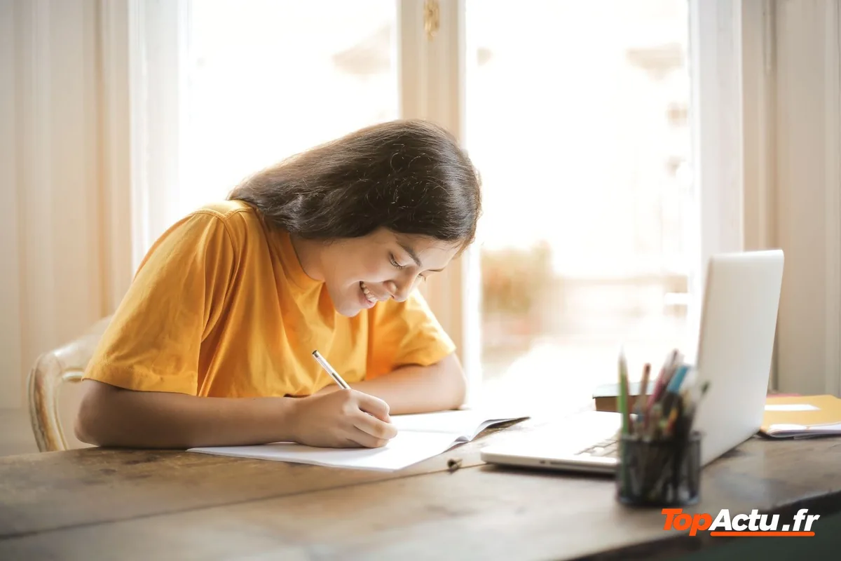 Élève qui écrit à la main devant un ordinateur portable