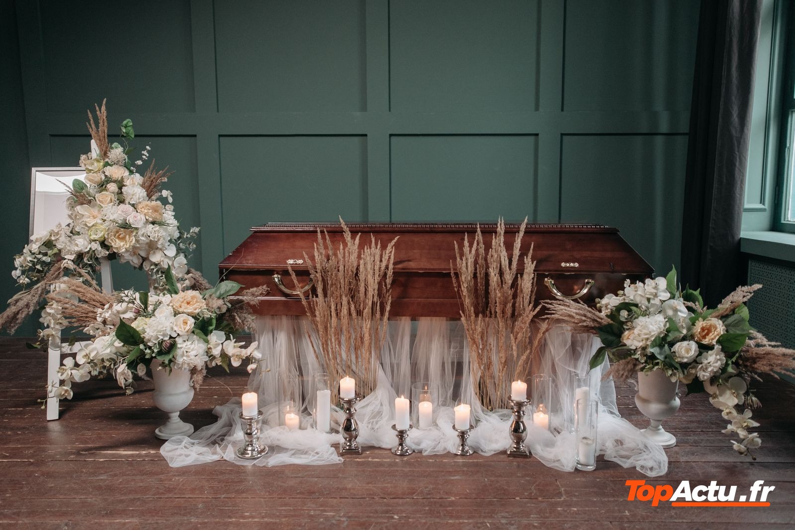 Cercueil entouré de fleurs et de bougies dans une salle