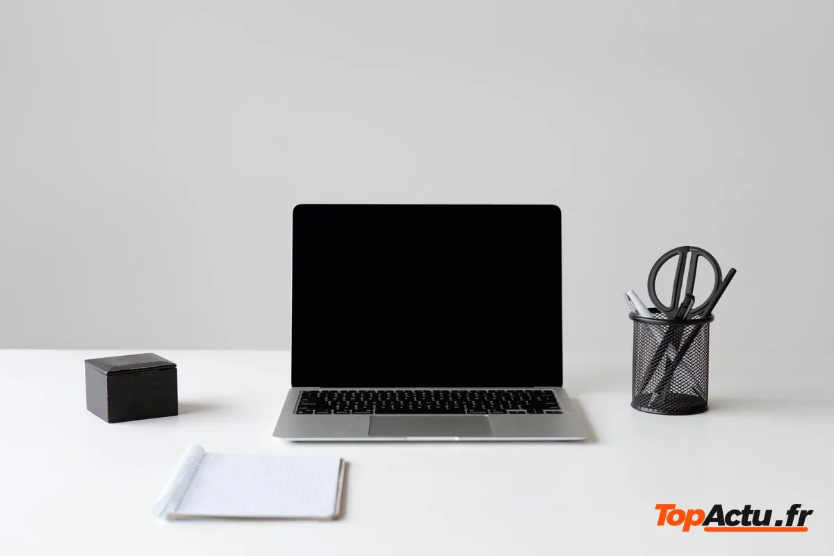 Un ordinateur portable ouvert sur un bureau blanc, à côté d'un pot à crayons