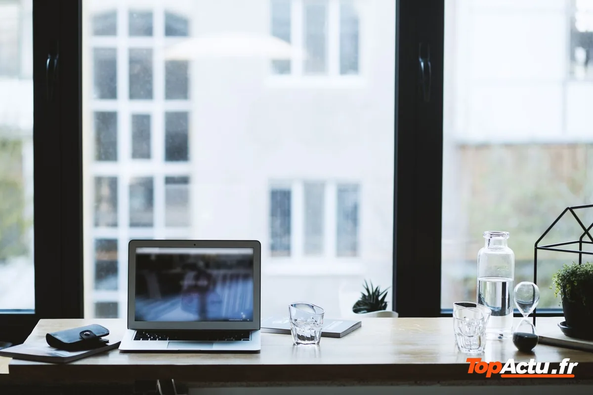 Un ordinateur portable ouvert sur un bureau devant une fenêtre