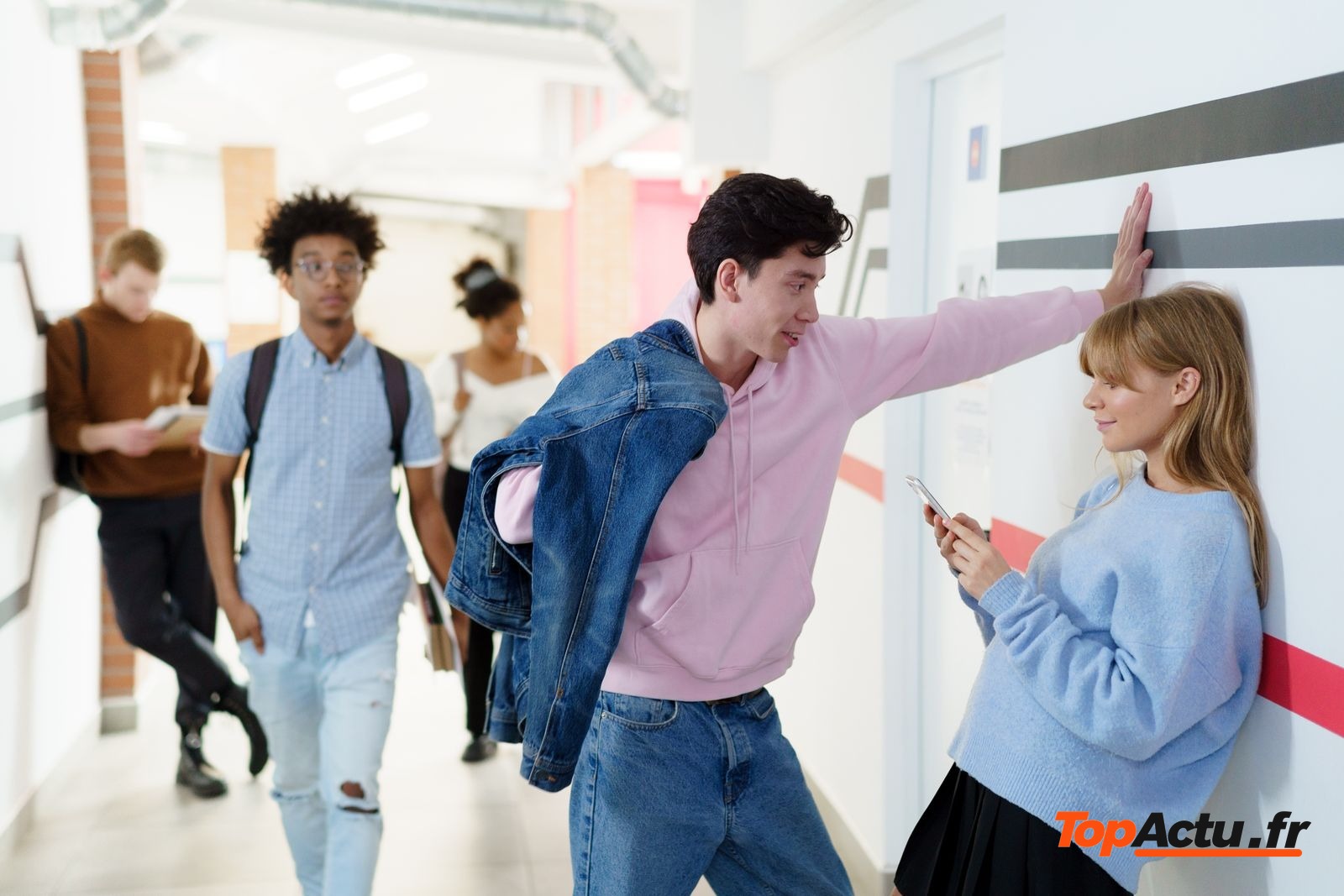 Lycéens dans un couloir de lycée, l'un d'eux regarde son smartphone