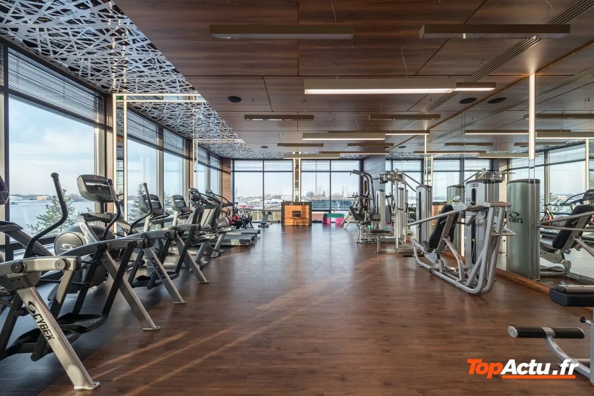 Salle de sport lumineuse aux grandes baies vitrées et au parquet, avec des appareils de cardio alignés