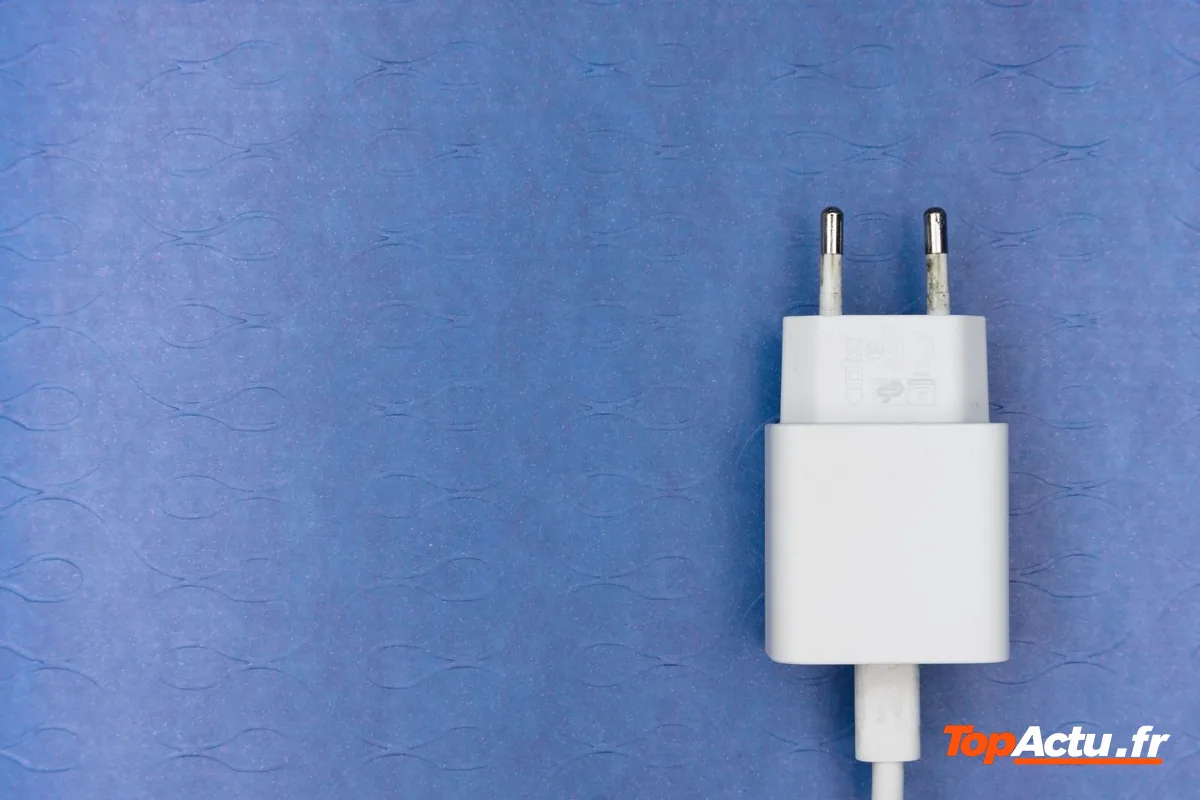 Un chargeur secteur blanc avec son câble sur un fond bleu