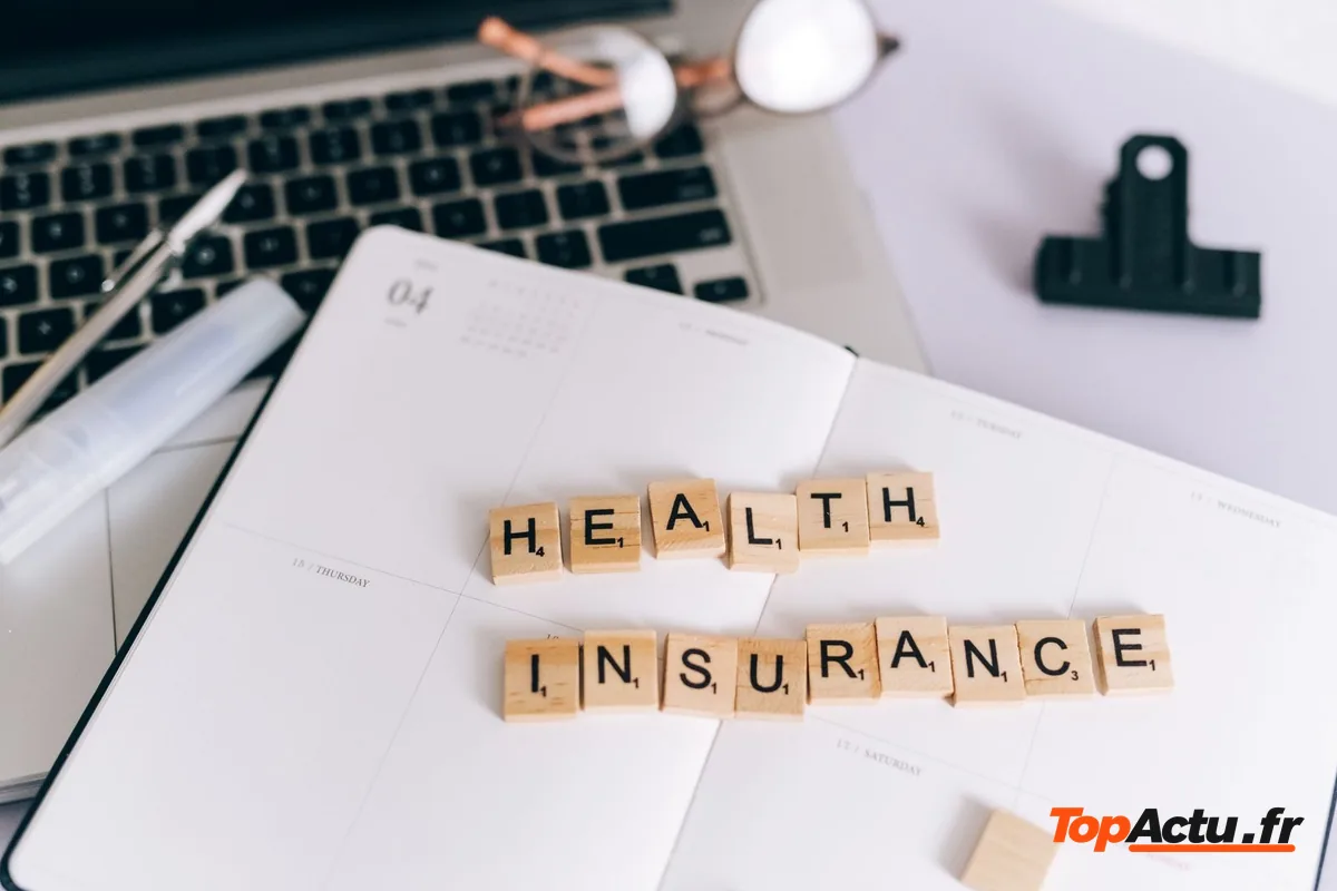 Lettres en bois formant les mots « health insurance » sur un carnet, près d'un ordinateur portable