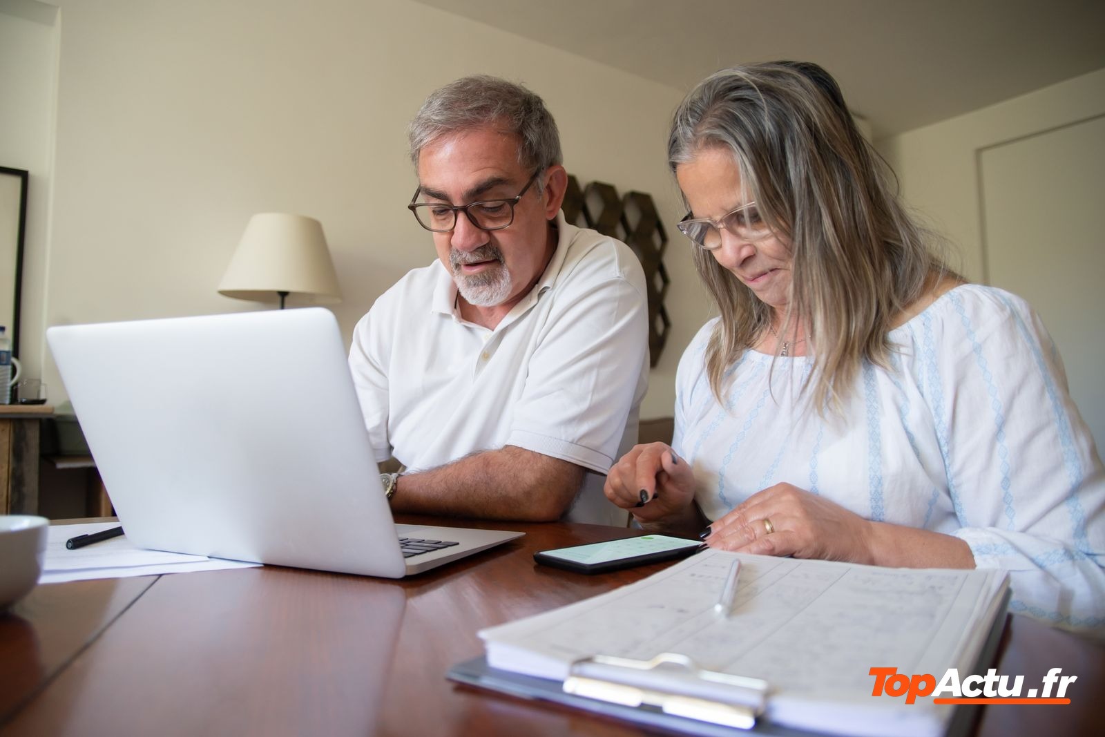 Couple de seniors devant un ordinateur portable, avec des documents posés sur la table