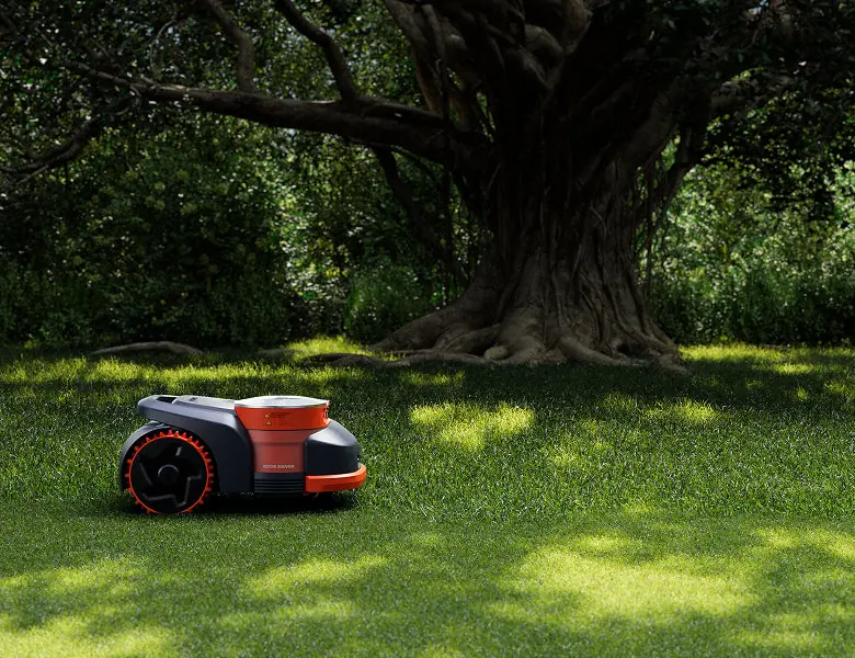 Une tondeuse robot Navimow qui tond sous un grand arbre, dans l'ombre et le soleil