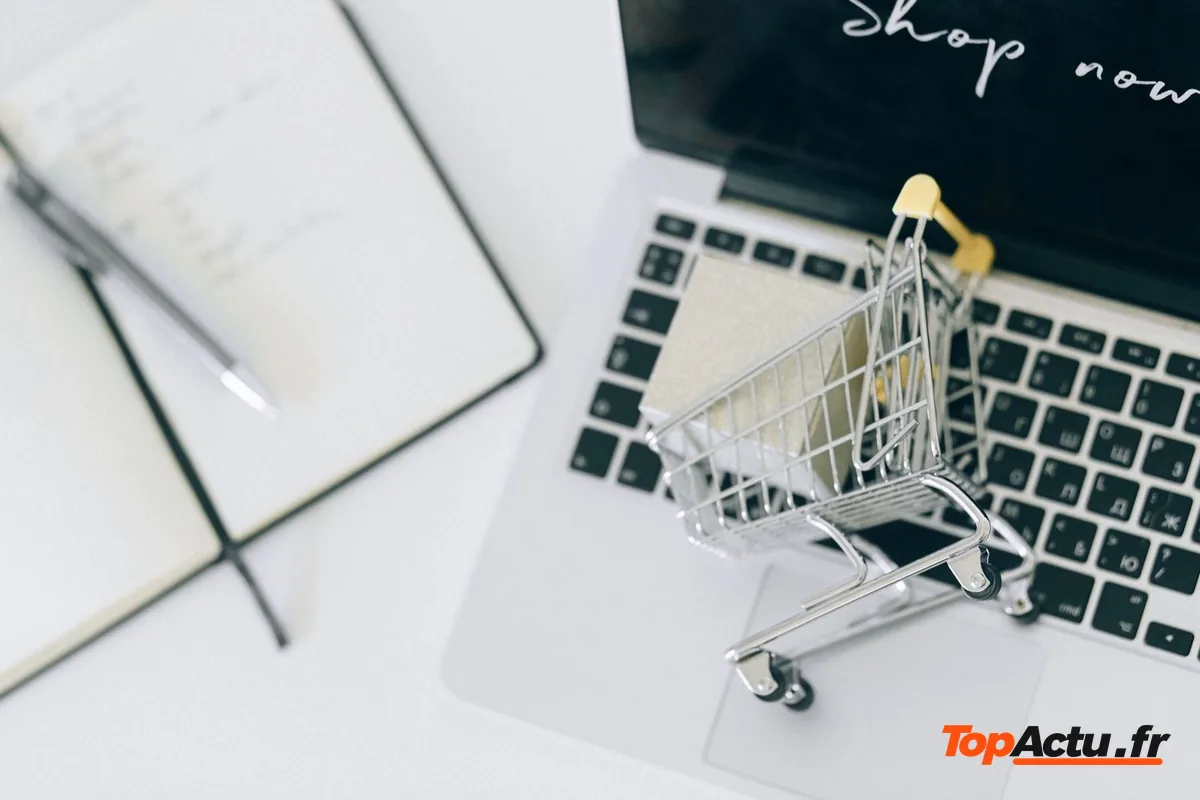 Petit chariot de magasin posé sur un clavier d'ordinateur, à côté d'un carnet