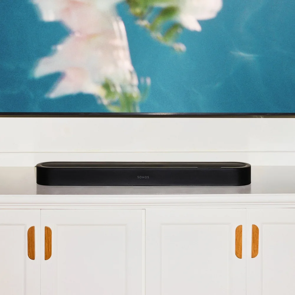 Barre de son Sonos Beam Ultra noire posée sur un meuble de télévision blanc, sous un téléviseur