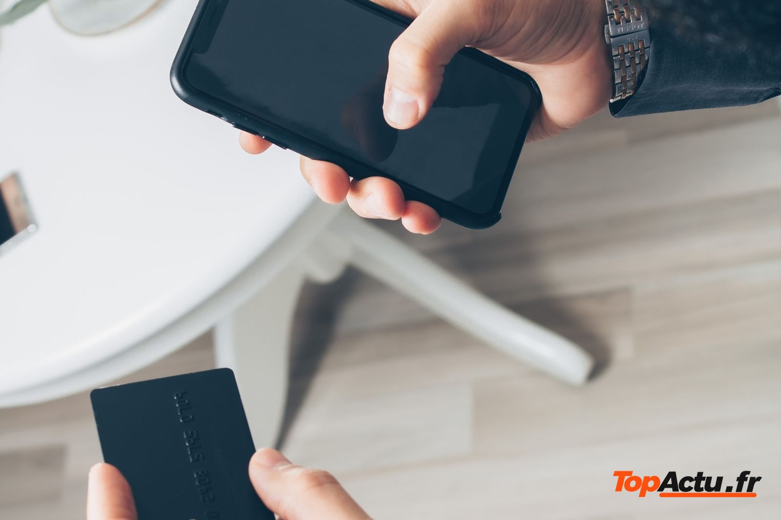 Mains qui tiennent un smartphone et une carte bancaire au-dessus d'une table