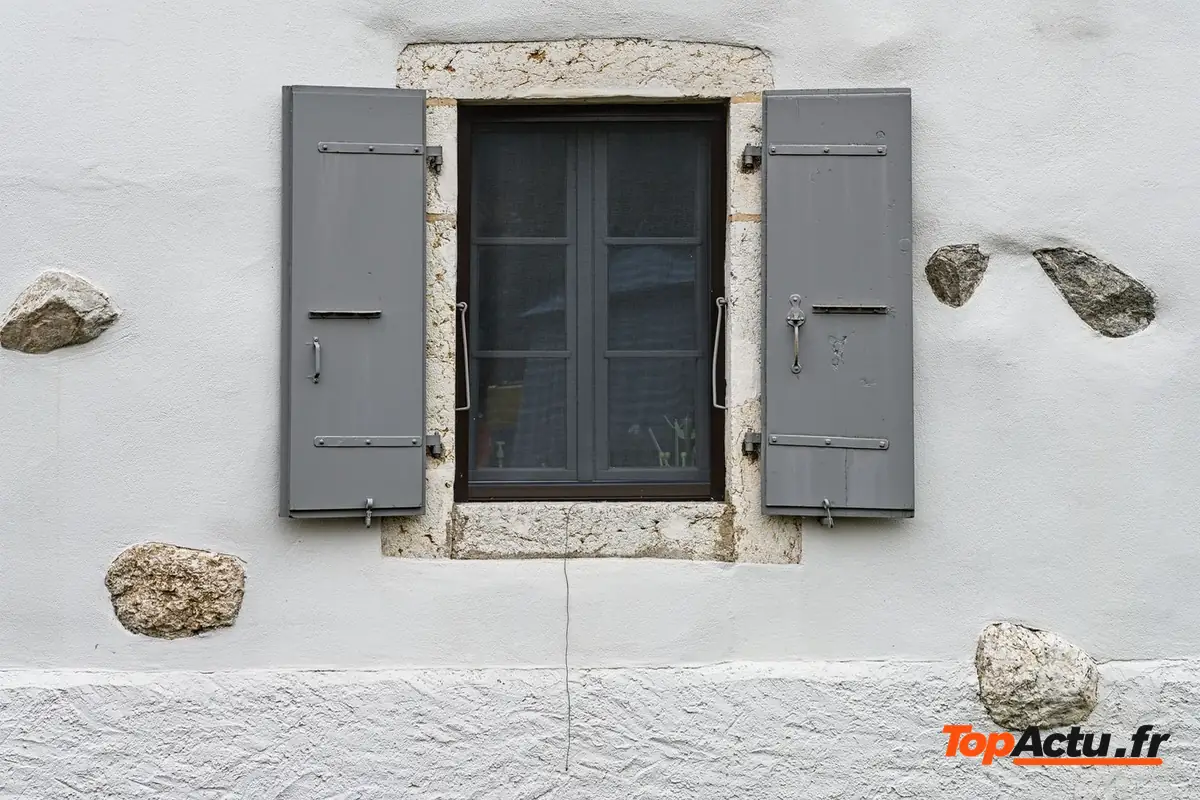 La façade en pierre d'une maison avec une fenêtre aux volets gris