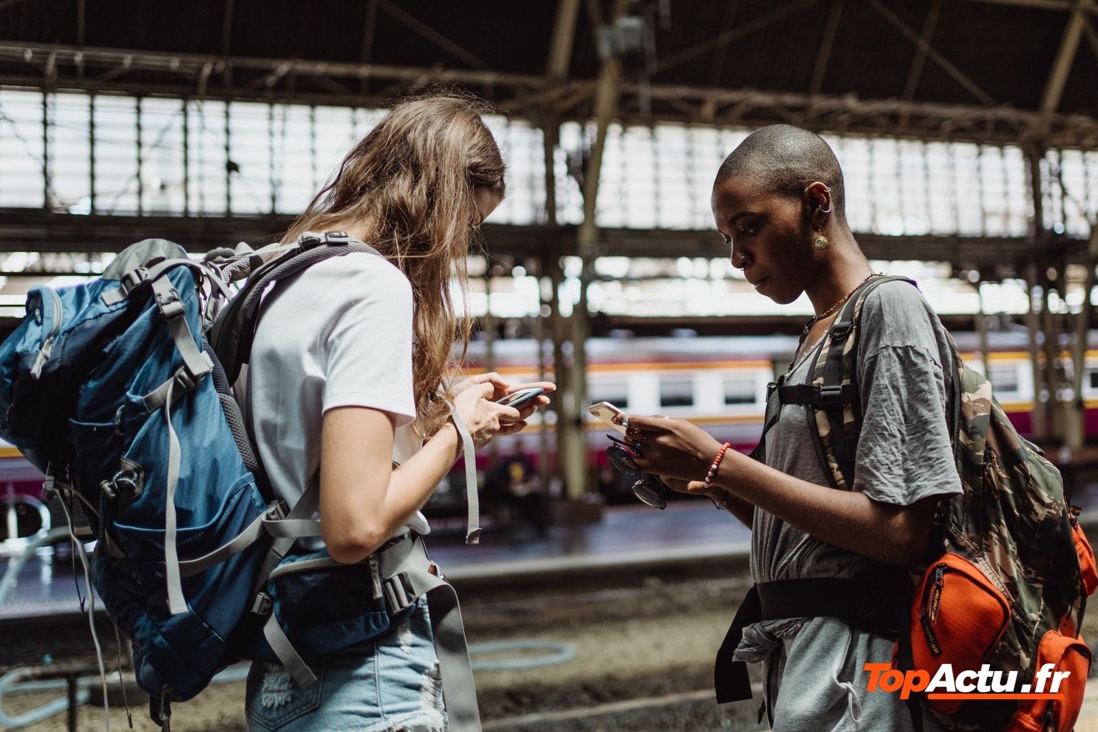 Deux voyageurs avec des sacs à dos qui regardent leur téléphone sur un quai de gare