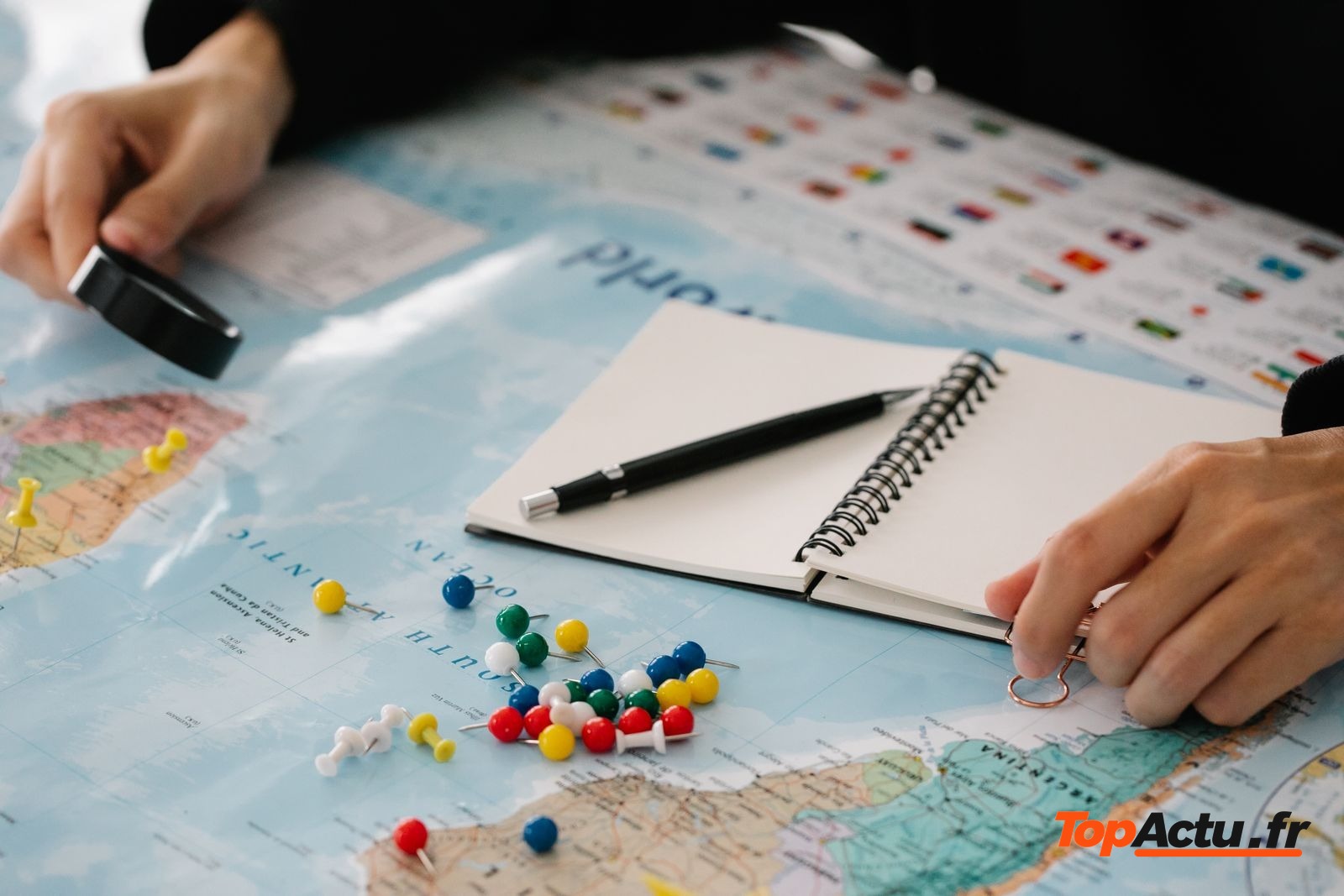 Carnet, stylo et carte du monde avec des épingles de couleur sur une table