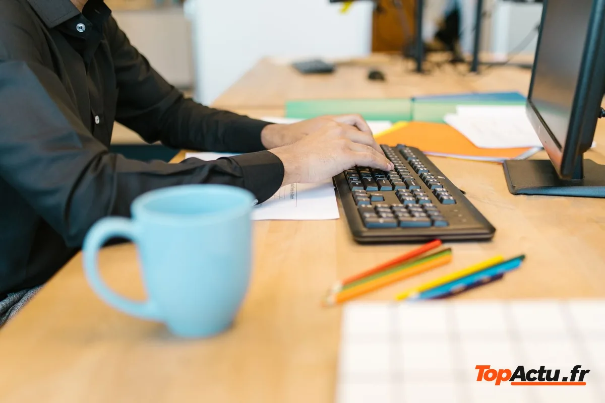 Mains sur un clavier d'ordinateur à côté d'une tasse bleue, sur un bureau en bois