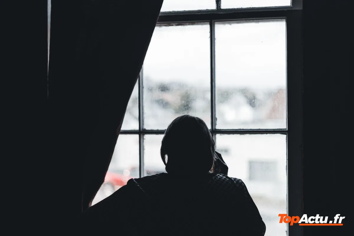 Silhouette d'une personne assise devant une fenêtre aux rideaux sombres