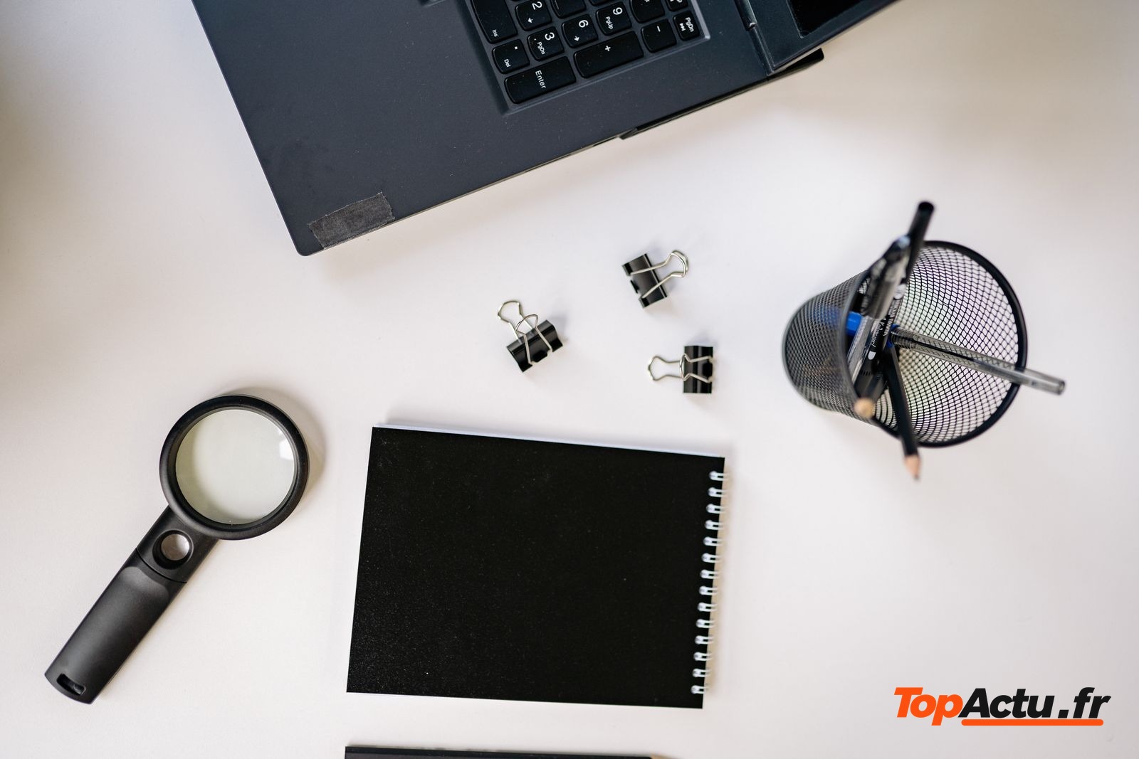 Loupe, carnet et ordinateur portable sur un bureau blanc